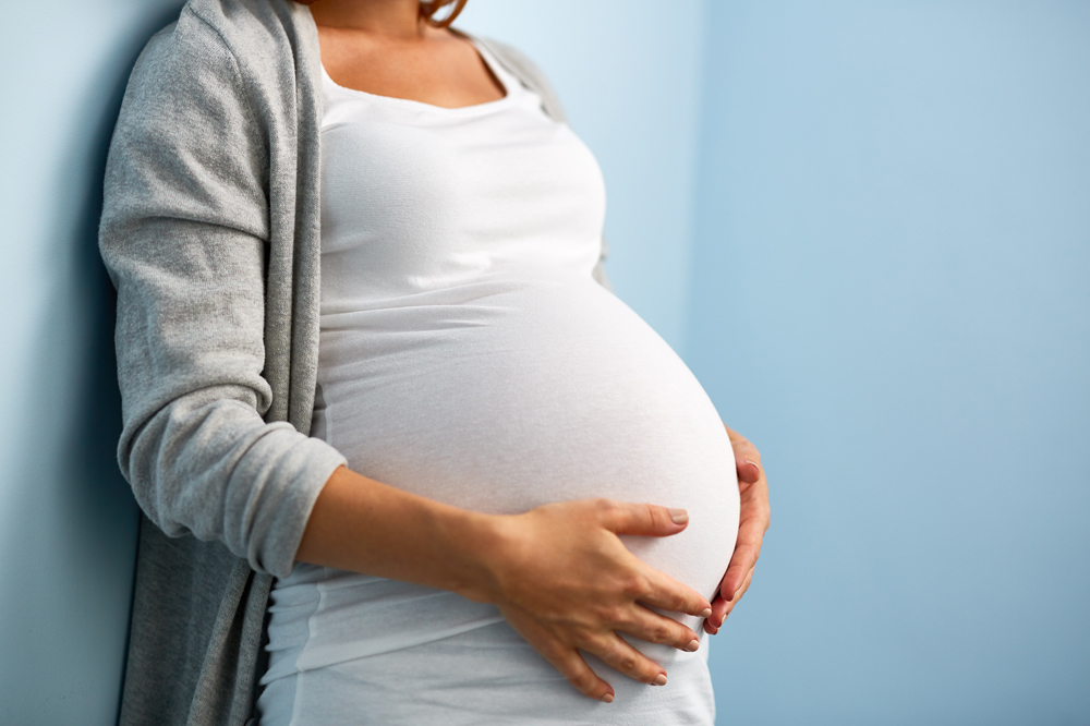 Eine schwangere Frau umfasst ihren Bauch mit beiden Händen