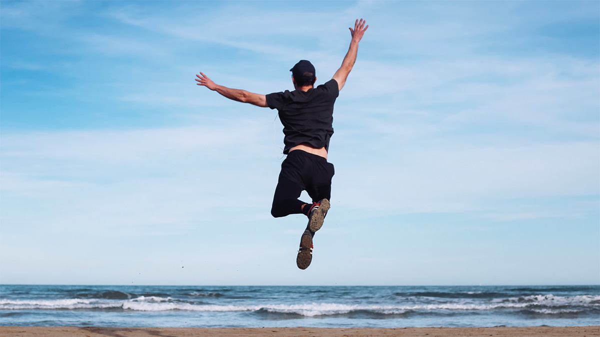 Junger Mann am Strand freudig in die Luft